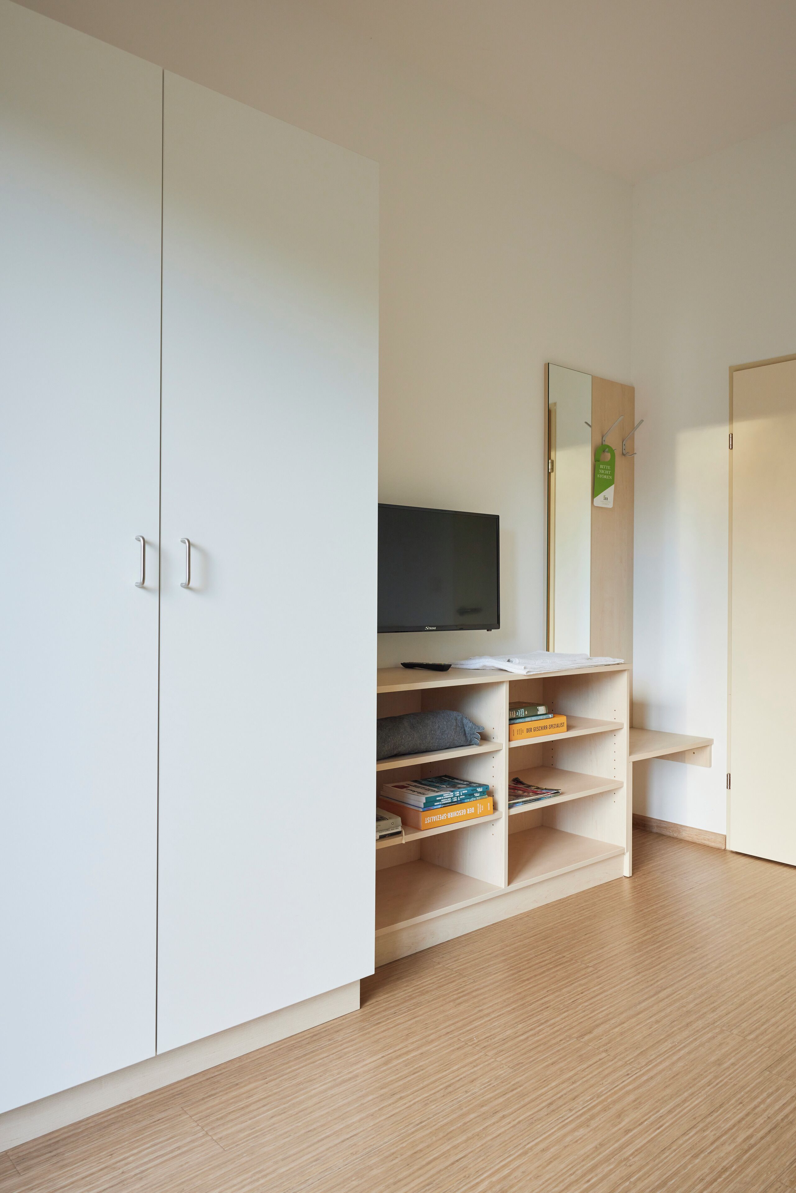 Een kamer met een witte kast, een televisie op een standaard, en een plank met boeken en een doos.