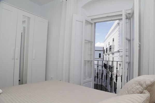 A bedroom with a bed, white walls, and a balcony with a railing.