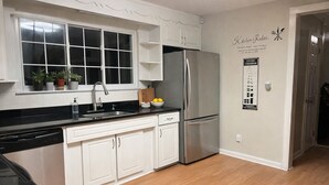 A kitchen with white cabinets, a stainless steel refrigerator, a black countertop, and a window above the sink.