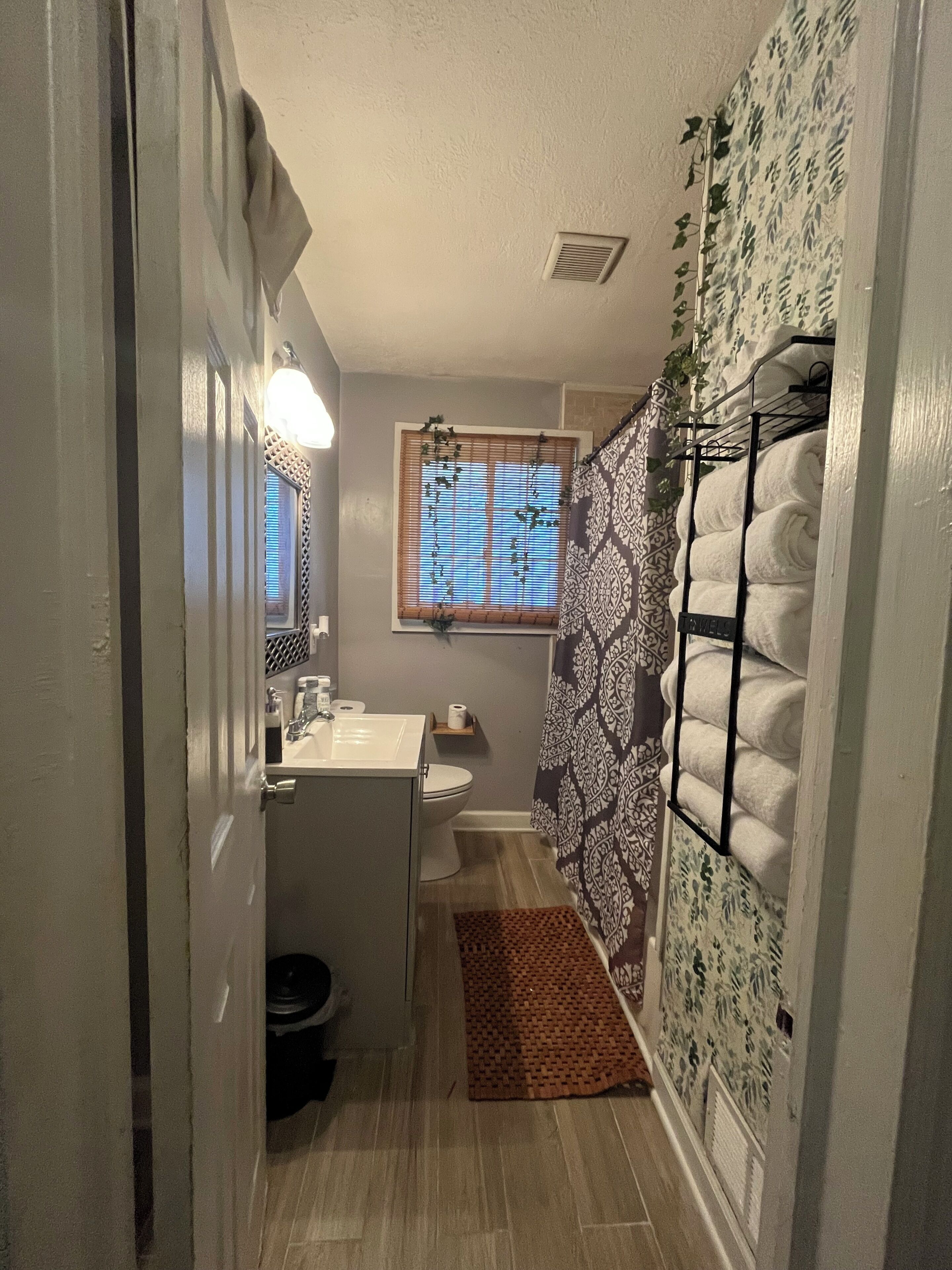 A narrow bathroom with a toilet, sink, and window with blinds.
