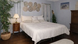 A bedroom with a bed, bedside table, lamp, decorative wall art, and a potted plant.