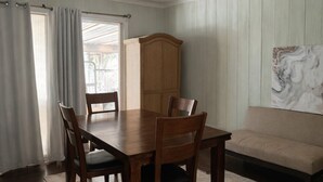 A dining area with a wooden table and chairs, a wooden cabinet, a beige sofa, and a painting on the wall.