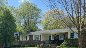 A single-story brick house with a front porch, a basketball hoop, and a well-maintained lawn.