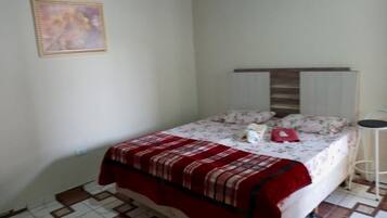 Una cama individual con colcha estampada y una manta roja, una mesita de noche y una lámpara de pie.