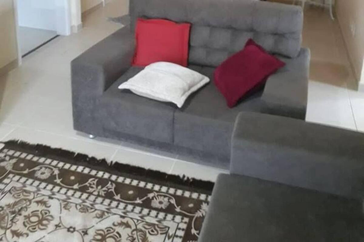 Ein Wohnzimmer mit grauem Sofa, einem gemusterten Teppich und einem Essbereich mit Tisch und Stühlen.