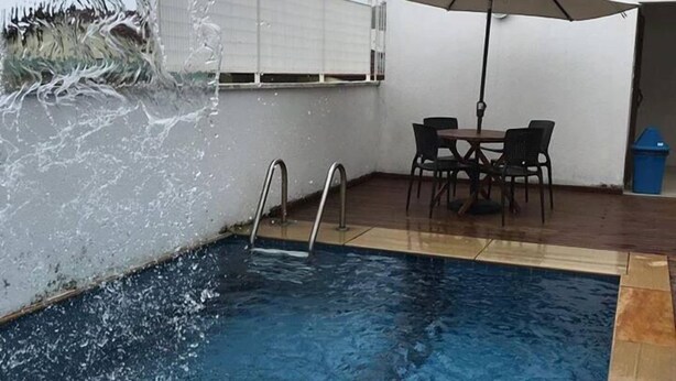 An indoor swimming pool with a water feature, a table with chairs, and a trash bin. - Hotel Fazenda Roseira Lagoinha (Ribeirão Preto)