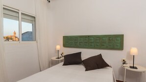 Ein Hotelzimmer mit einem Bett, zwei Nachttischen mit Lampen, einem Fenster mit Vorhängen und einer grünen Wanddekoration.