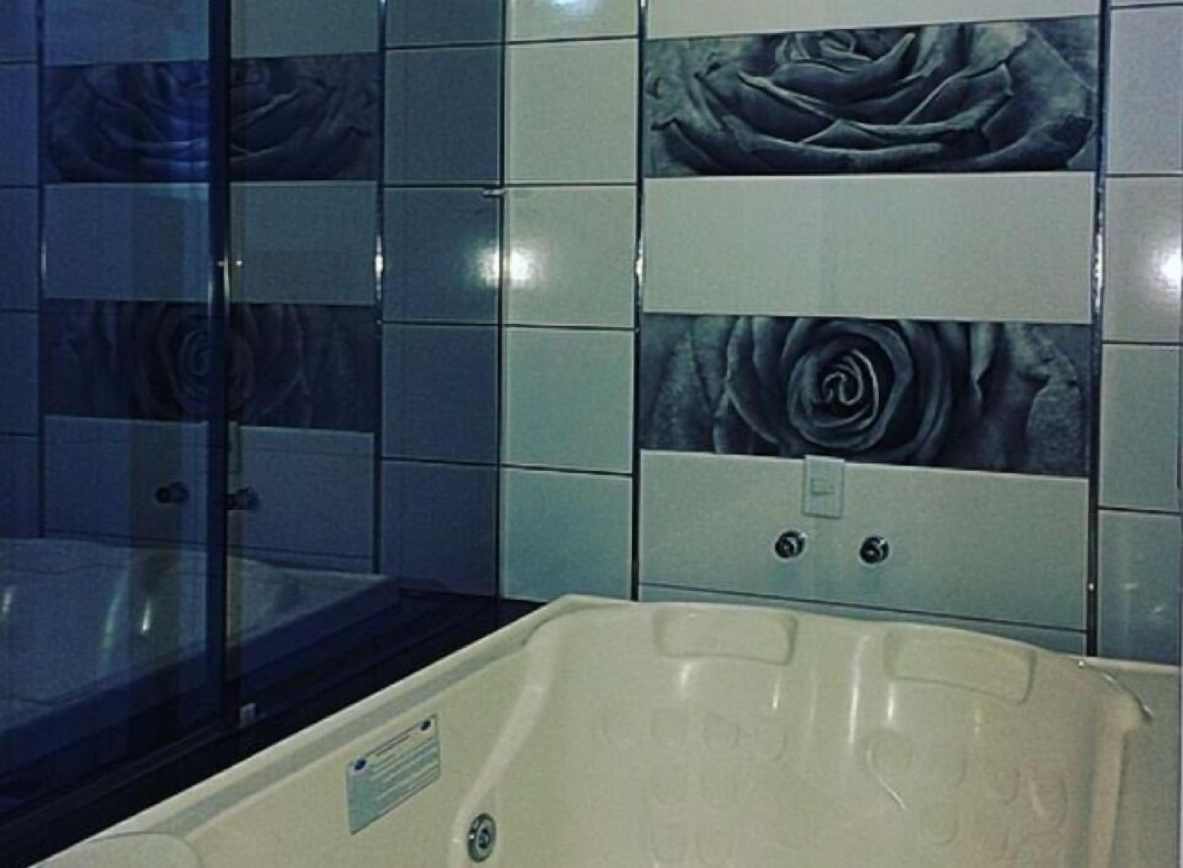 Un bagno con una vasca, un box doccia in vetro e piastrelle decorative con motivo floreale a forma di rosa.