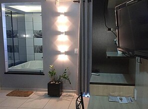 A modern bathroom with a glass shower enclosure, a potted plant, and a television mounted on the wall.