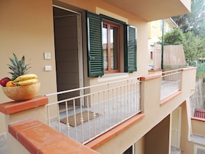 A balcony with a wooden bowl of fruit, a window with green shutters, and a door.