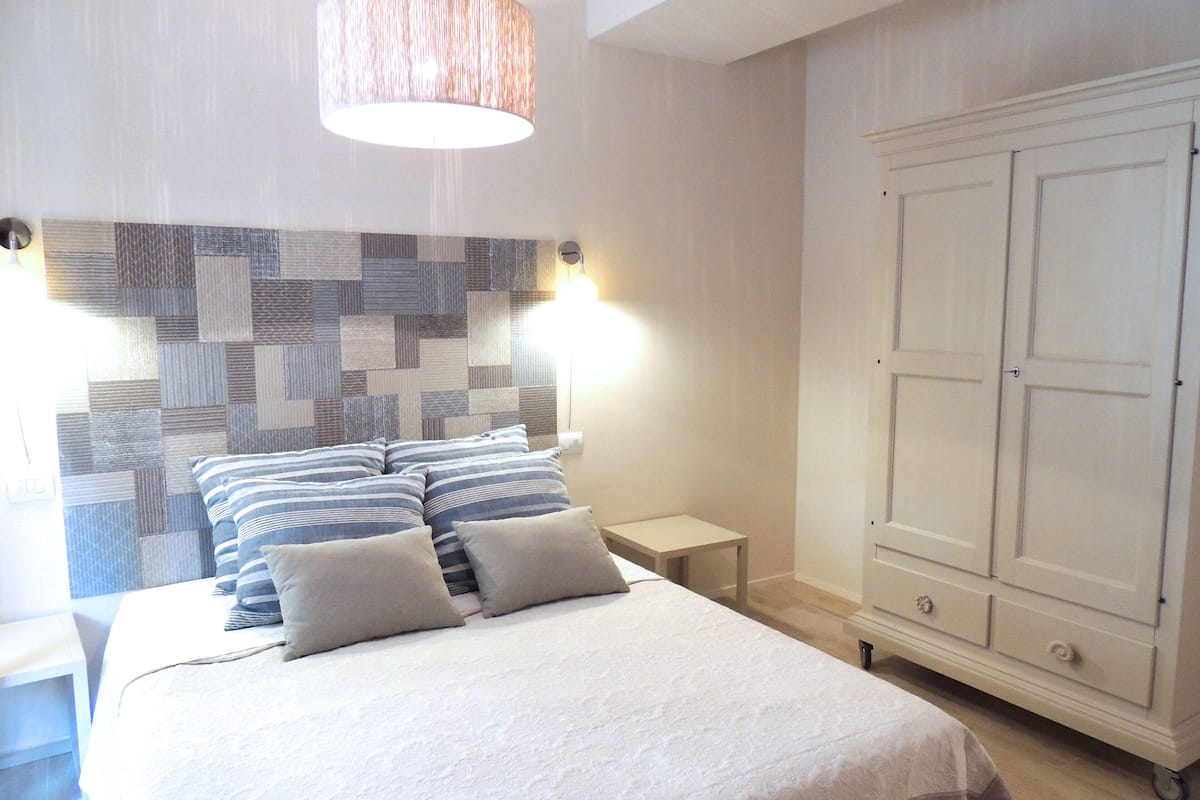 A bedroom with a bed, a headboard with a geometric pattern, a bedside table, and a wardrobe.