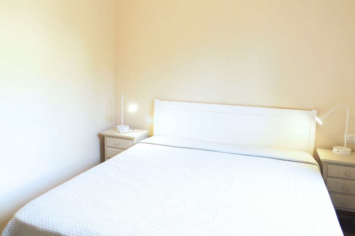 A simple, well-lit bedroom with a single bed, two bedside tables, and two lamps.
