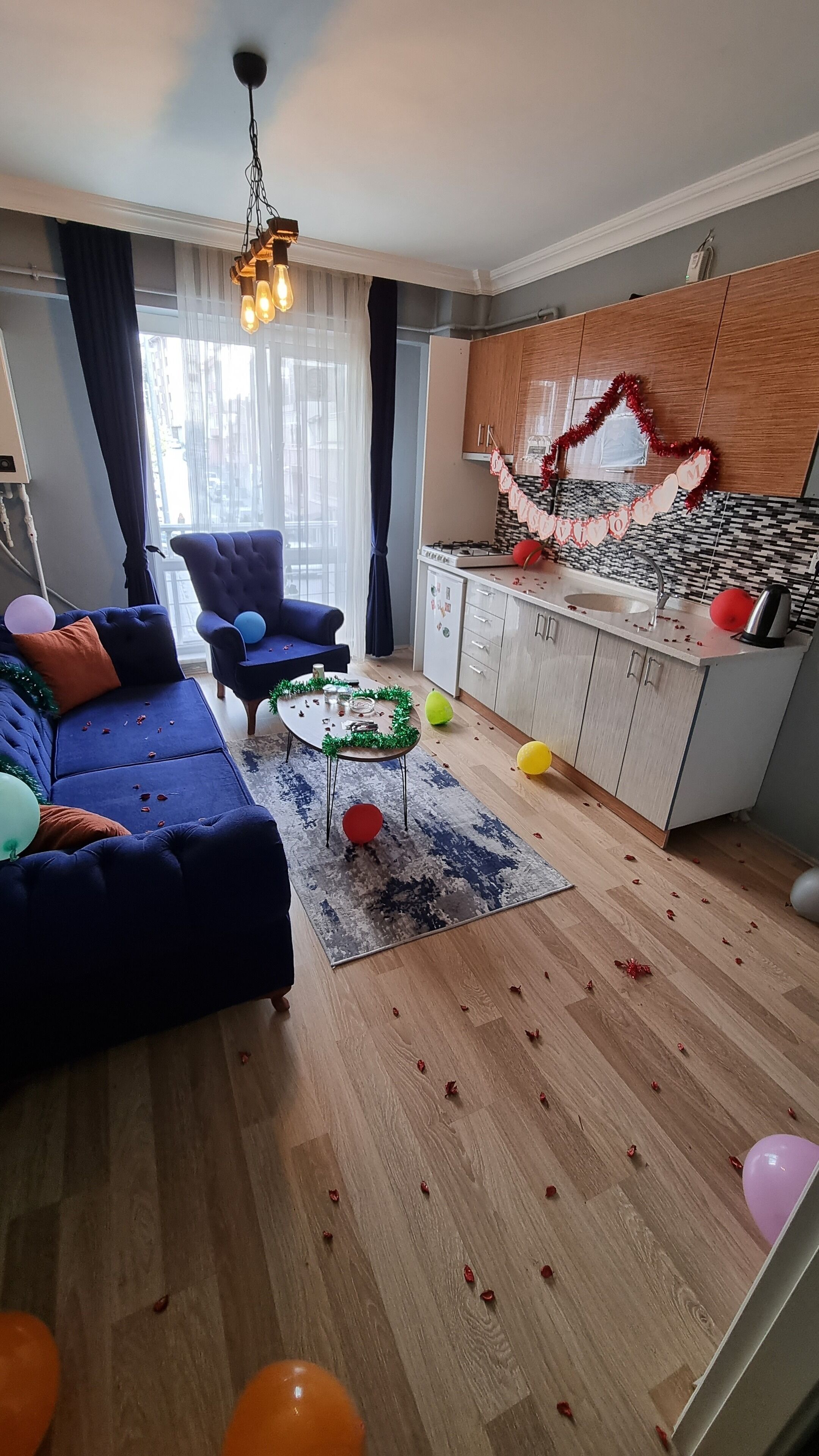 Una sala de estar con un sofá, un sillón y una mesa de centro. Hay una zona de cocina con un refrigerador y un lavadero.