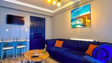 Una sala de estar moderna con un sofá azul, una mesa de centro de madera y un televisor montado en la pared.