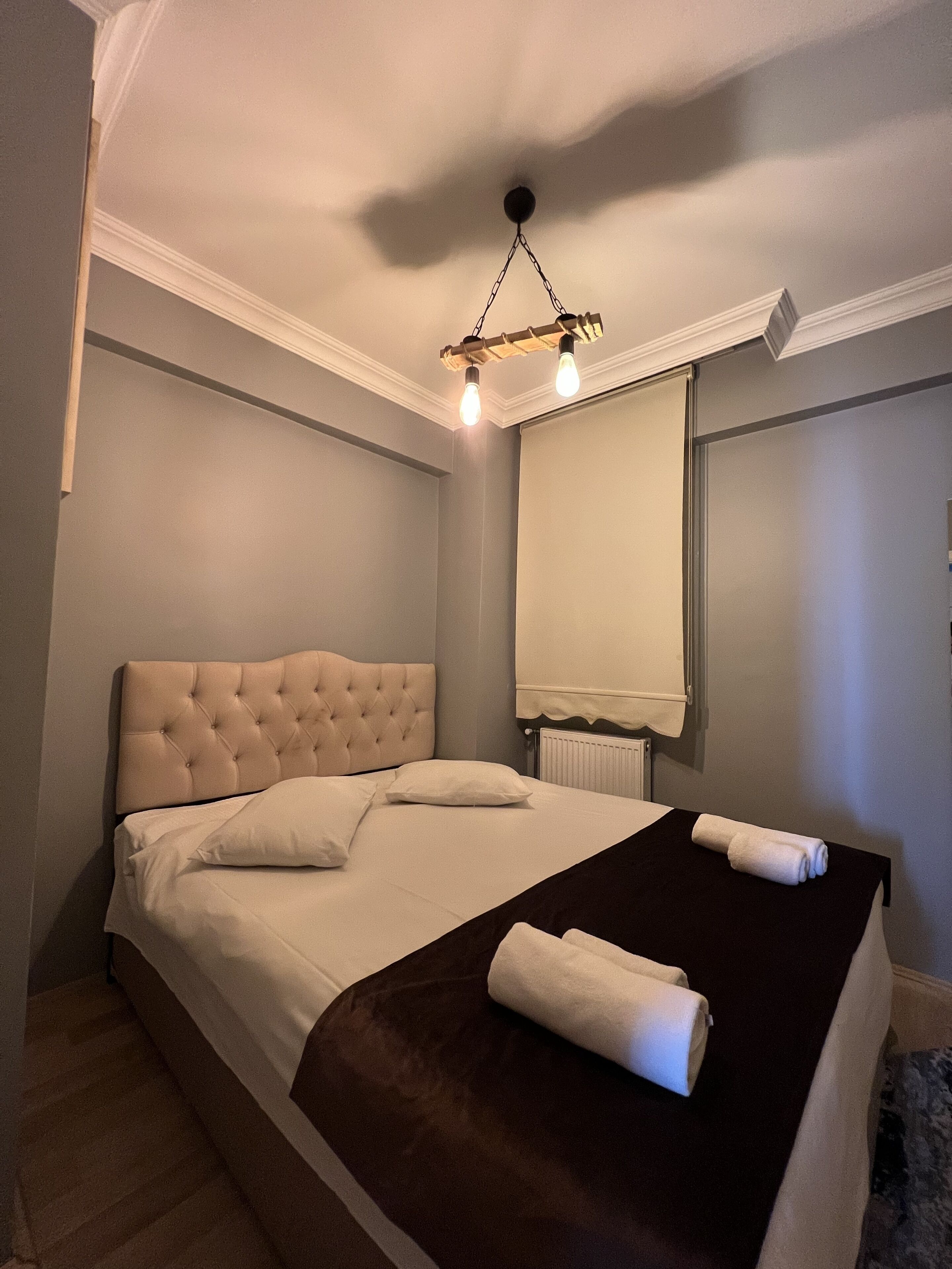 A neatly made bed with a tufted headboard, a black throw blanket, and a rolled towel.
