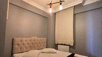 A neatly made bed with a tufted headboard, a black throw blanket, and a rolled towel.