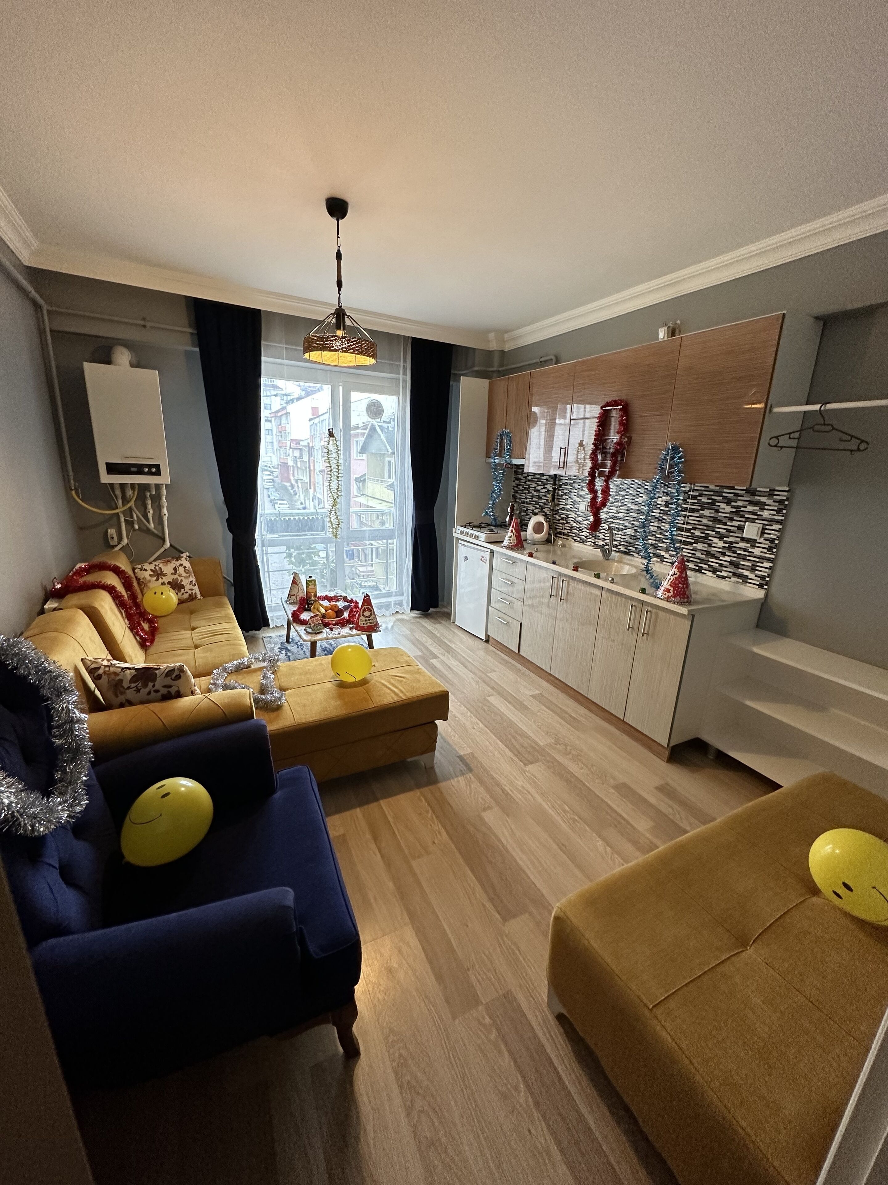 A modern living room with a sofa, ottoman, and a dining area with a kitchen in the background.