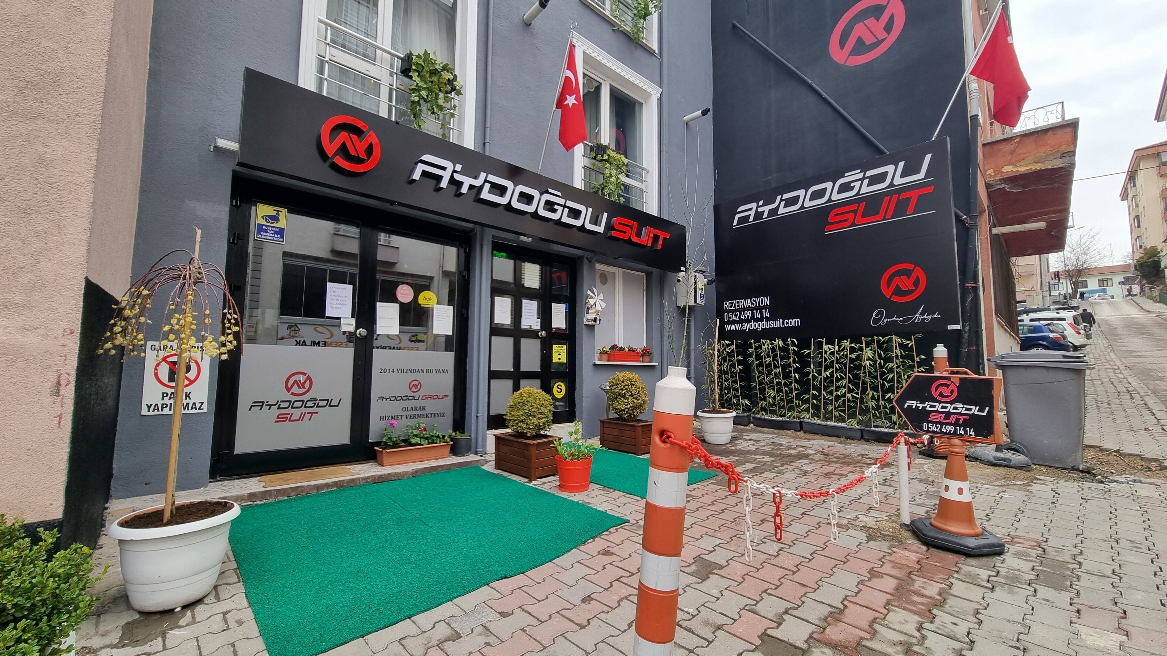 Une devanture de magasin avec un auvent noir, un tapis vert et un panneau indiquant une zone où le stationnement est interdit.