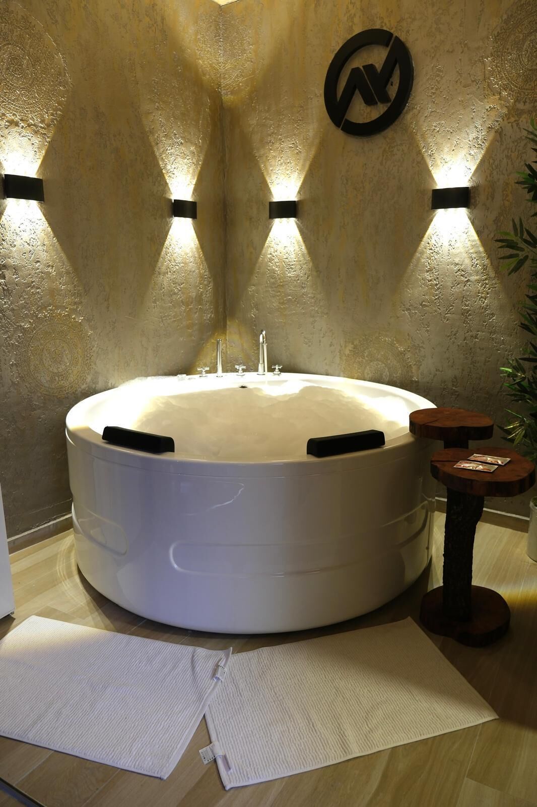 A large, round bathtub with a white interior, surrounded by a textured wall with a logo.