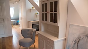 Une pièce comprenant un fauteuil recouvert d’un tissu gris, un meuble blanc aux portes vitrées et un tableau accroché au mur.