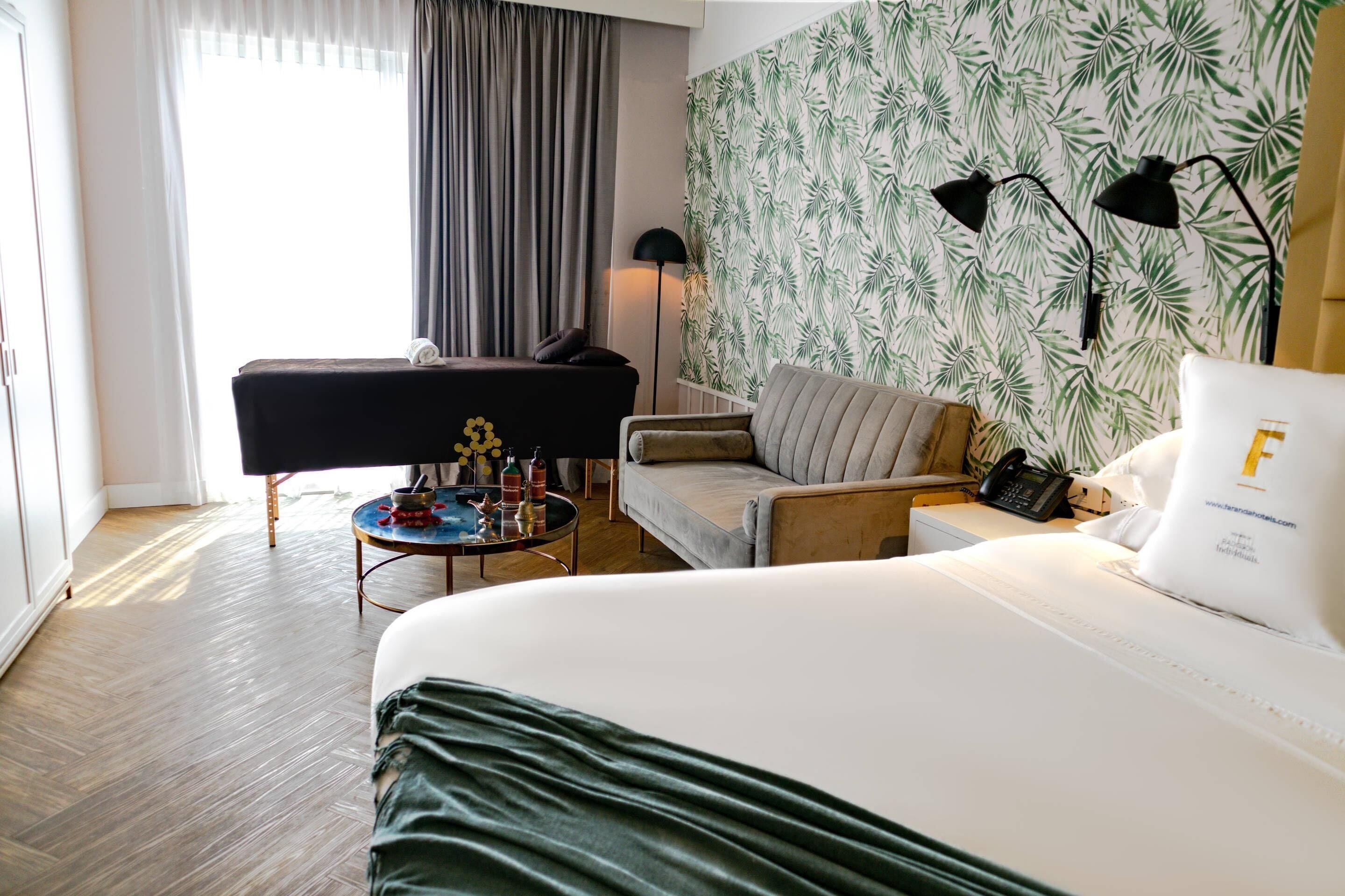 Habitación de hotel con cama, sofá, una mesita con bebidas, lámpara y pared con diseño.