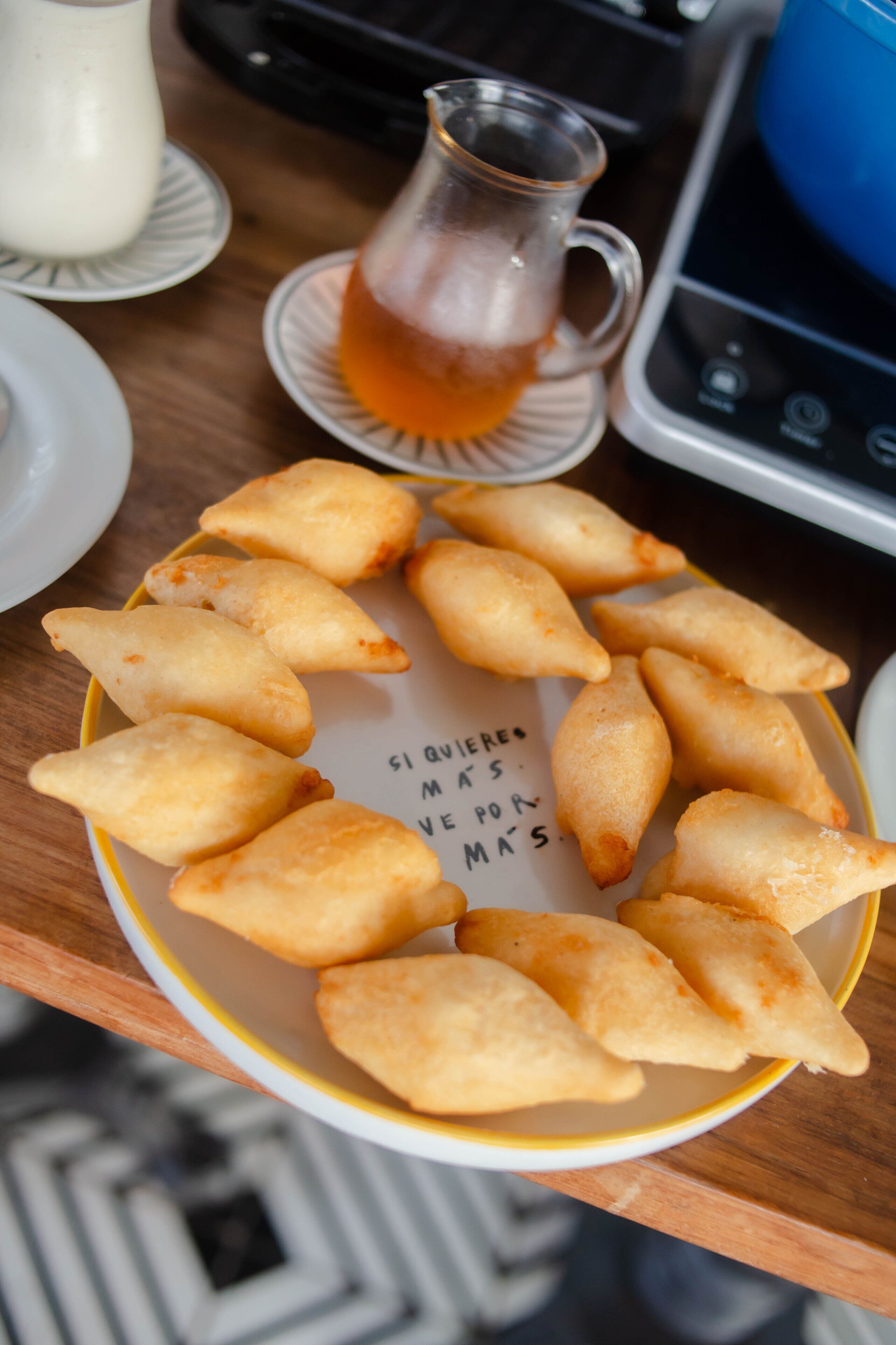 A plate of golden-brown pastries arranged in a circle on a table with a cup of tea in the background.