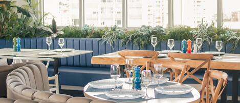 A restaurant with round tables, blue upholstered seating, and large windows offering a city view.