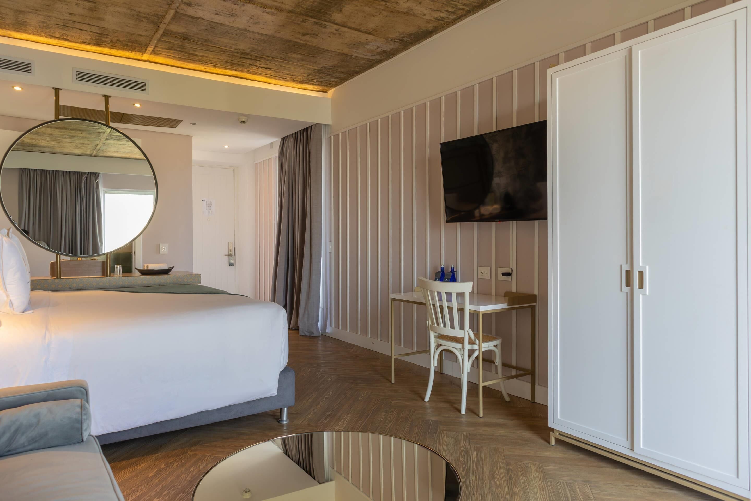 A hotel room with a bed, a desk, a chair, a TV, and a wardrobe.