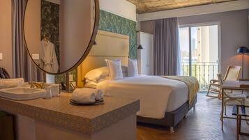 A hotel room with a bed, a desk, a chair, a round mirror, a sink, and a window with a view.