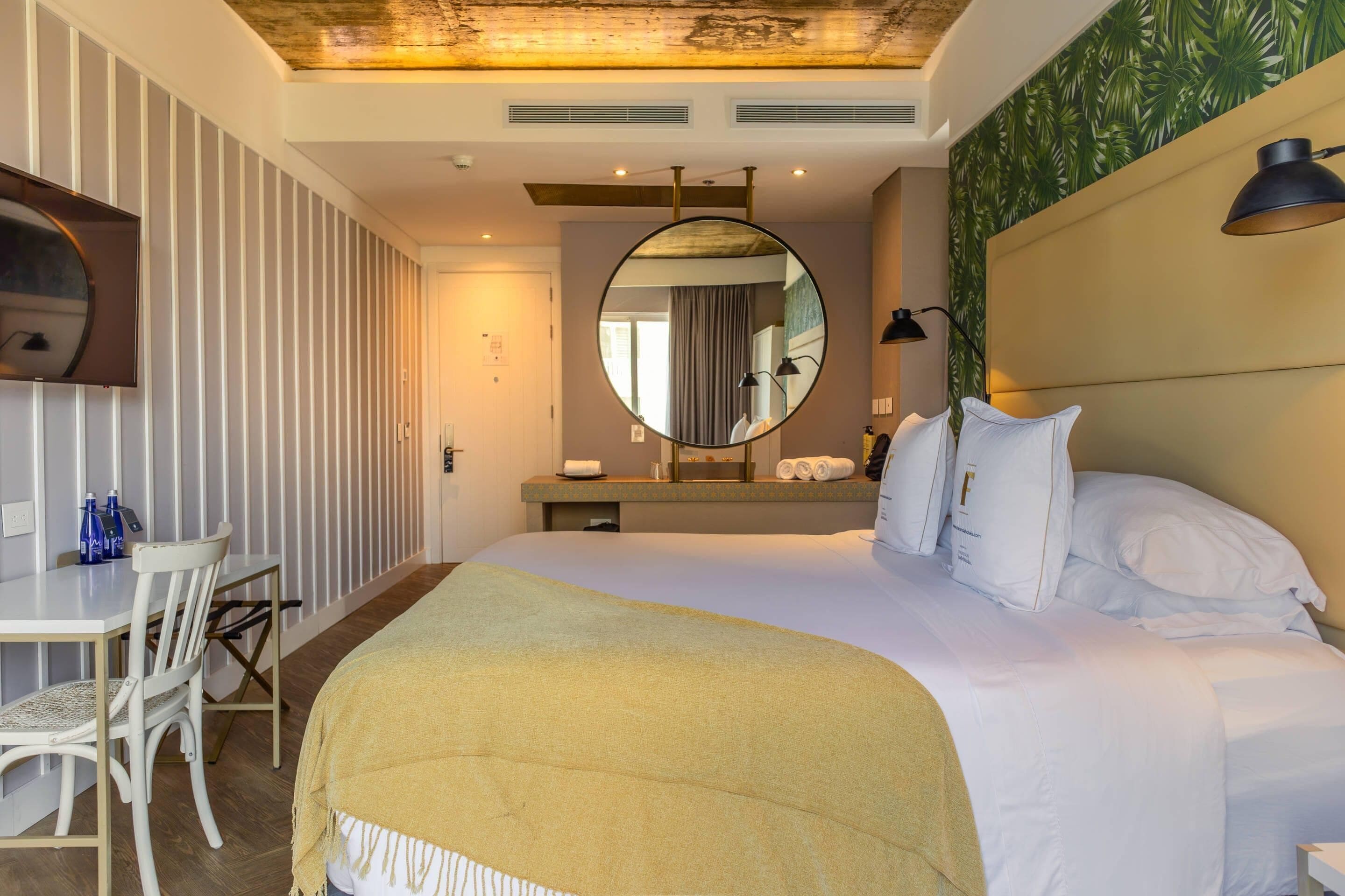 A hotel room with a bed, a desk with chairs, a mirror, and a television.