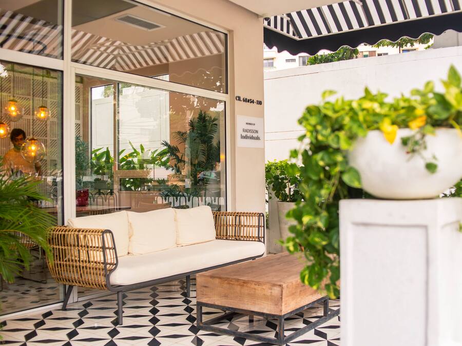 A modern outdoor seating area with a sofa and a wooden table, surrounded by potted plants and a patterned floor.