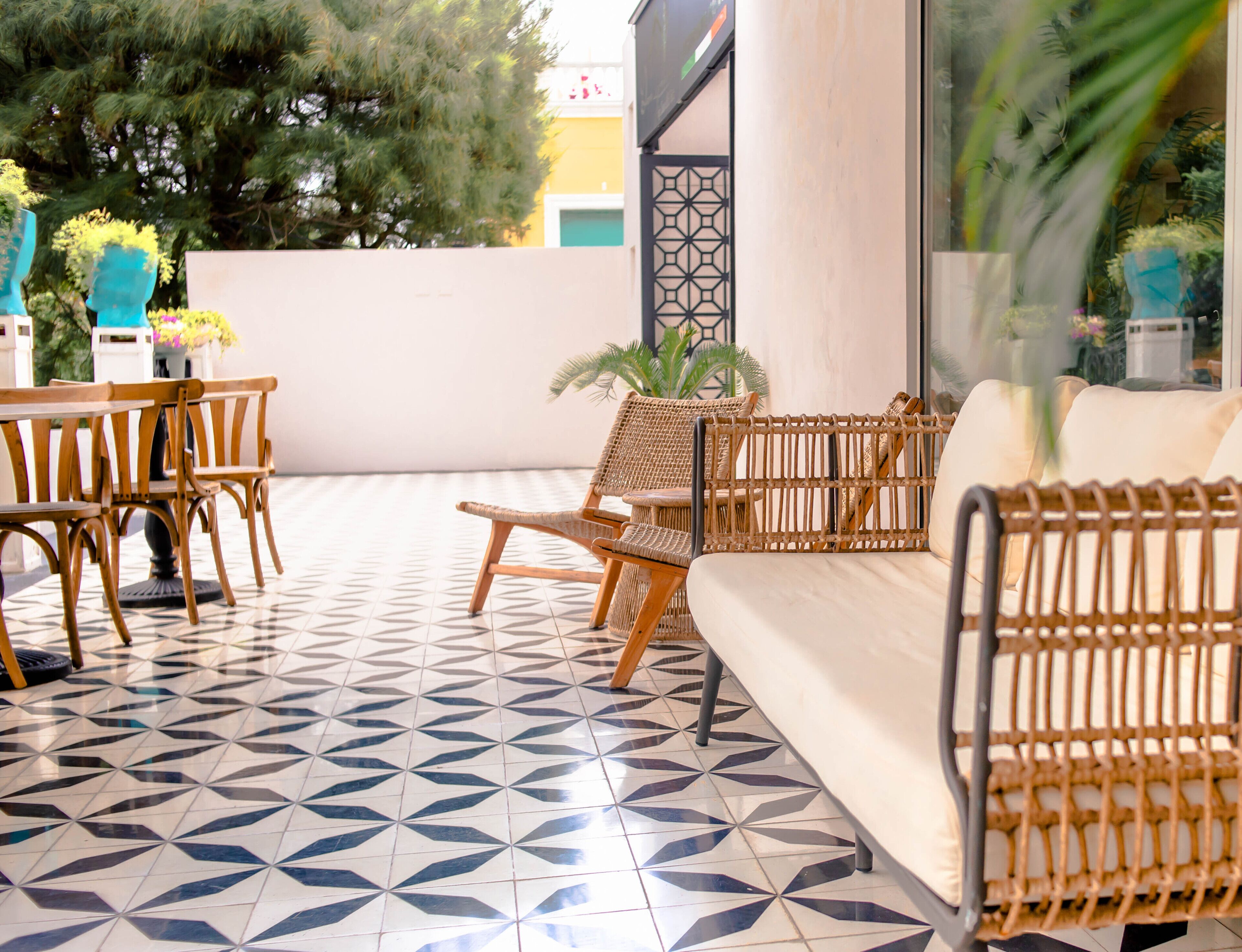 A sunlit patio with a geometric tile floor, wicker furniture, and potted plants.