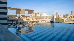 Une piscine sur le toit, dotée de chaises longues et offrant une vue sur la ville.