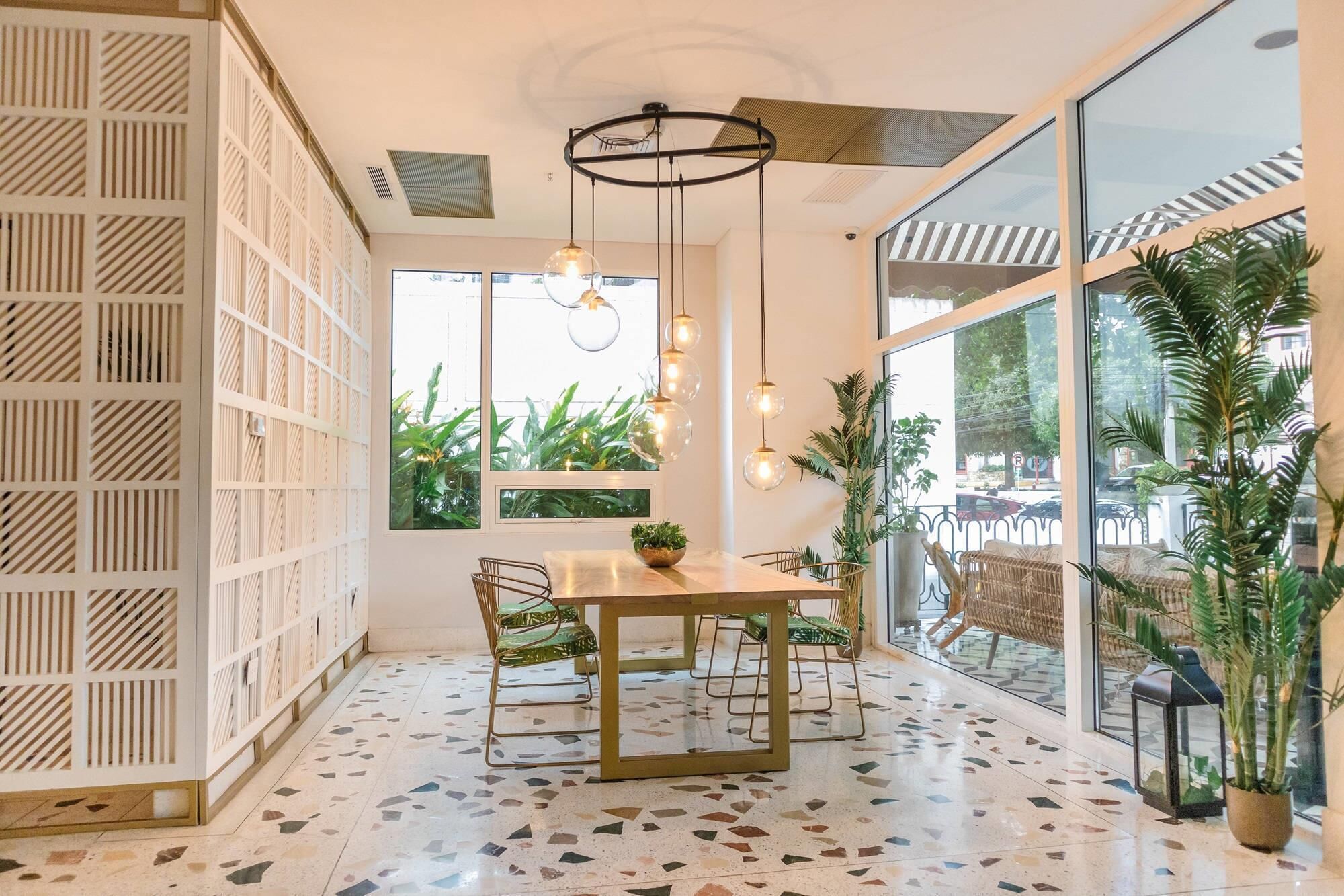 A modern dining area with a terrazzo floor, a wooden dining table, and chairs. There are large windows with a view of greenery outside.