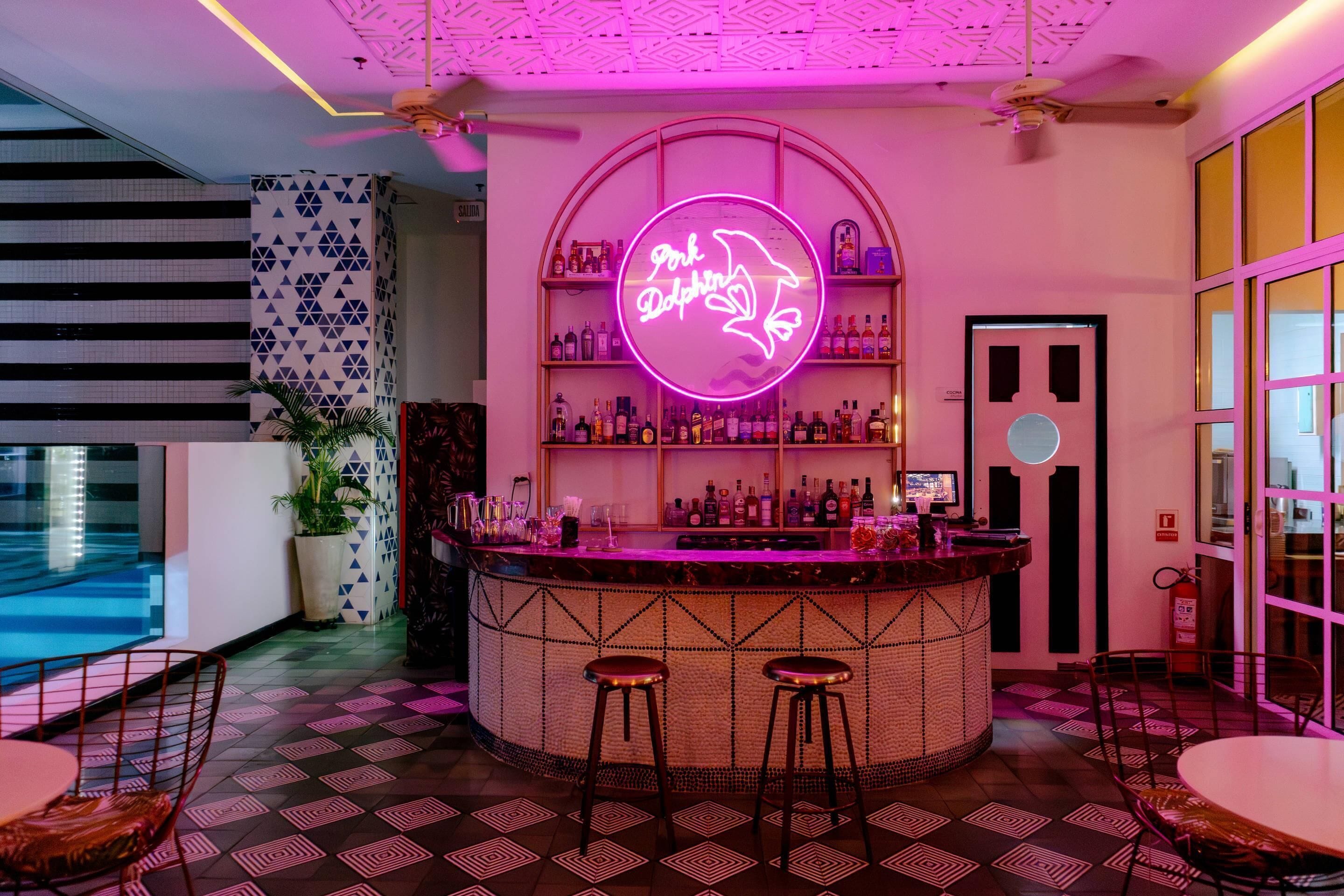 A bar area with a neon sign, a pool, and a patterned floor.