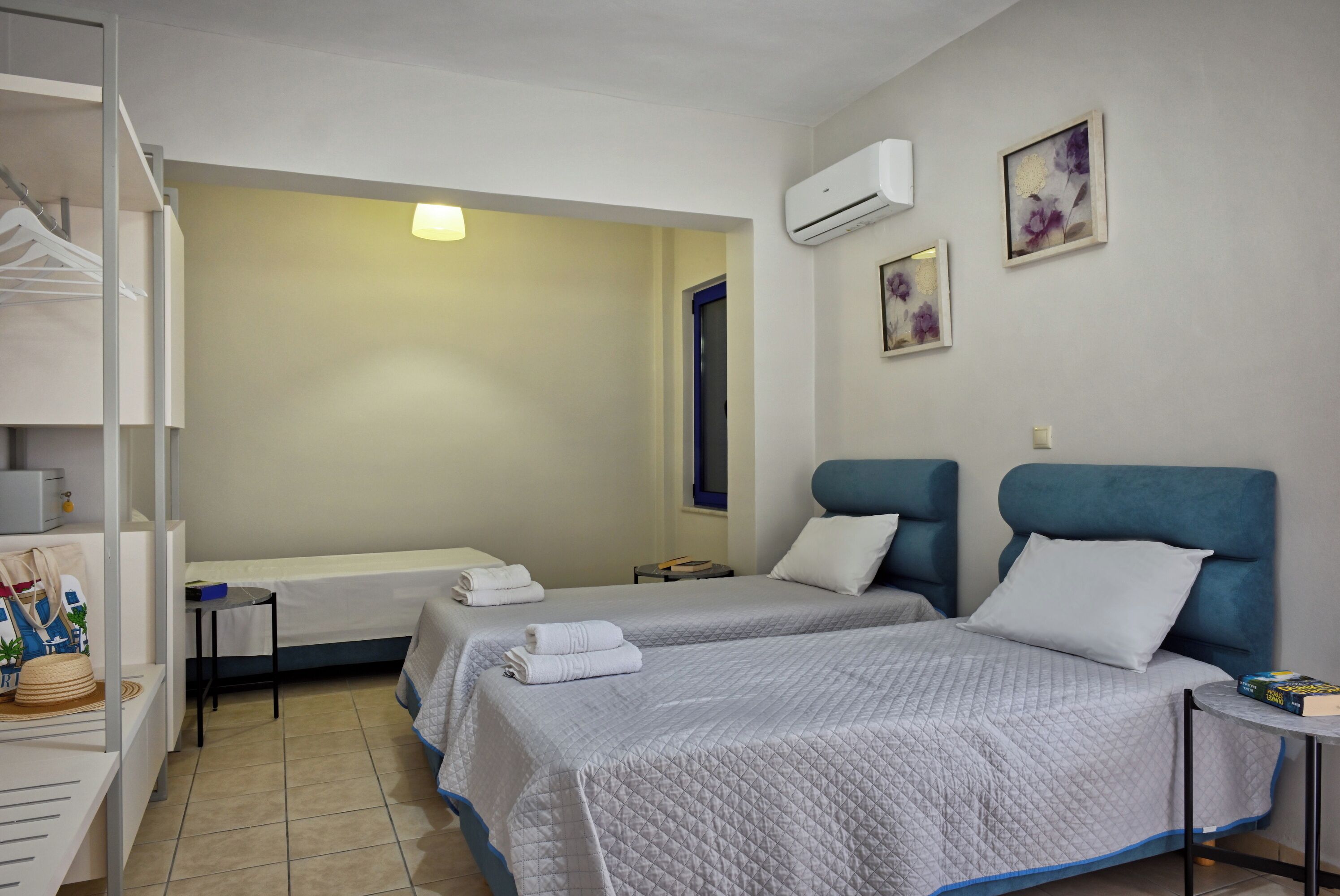 Habitación de hotel con dos camas, un armario, una mesita de noche y una pequeña mesa con un libro.