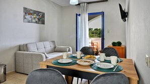A dining area with a wooden table set for two, a grey sofa, and a painting on the wall. - Sfakian Horizon (Sfakia)