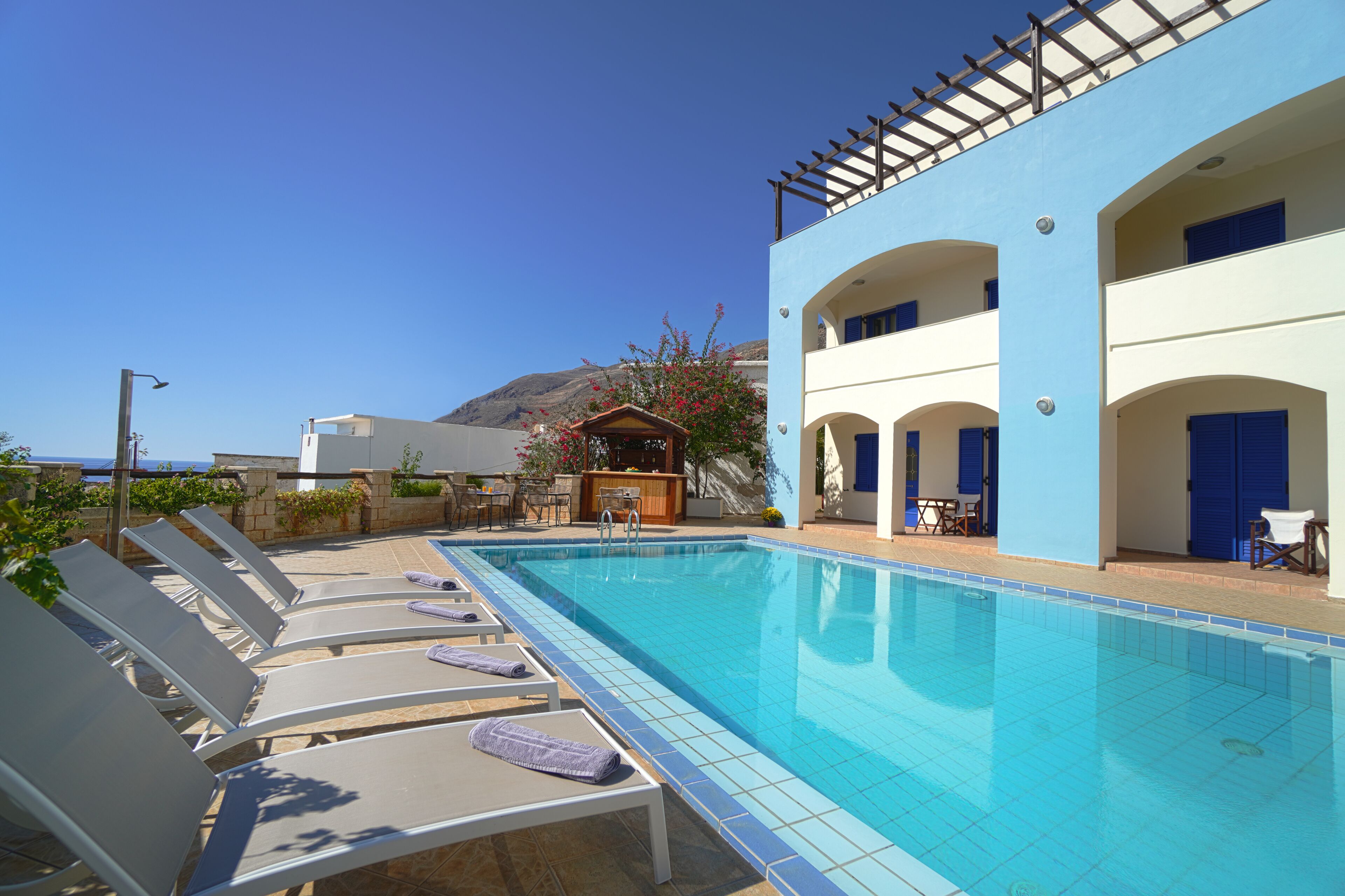 Area piscina con sedie a sdraio, una piscina, un bar e vista sul mare.