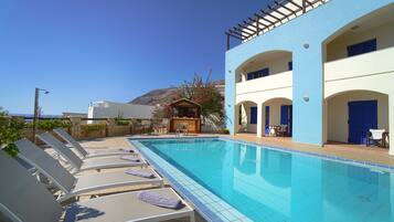 Un espace aménagé au bord de la piscine, avec des chaises longues et une piscine, un bar, et une vue sur la mer.