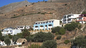 A hillside with buildings, including a blue and white structure with multiple balconies. - Sfakian Horizon (Sfakia)