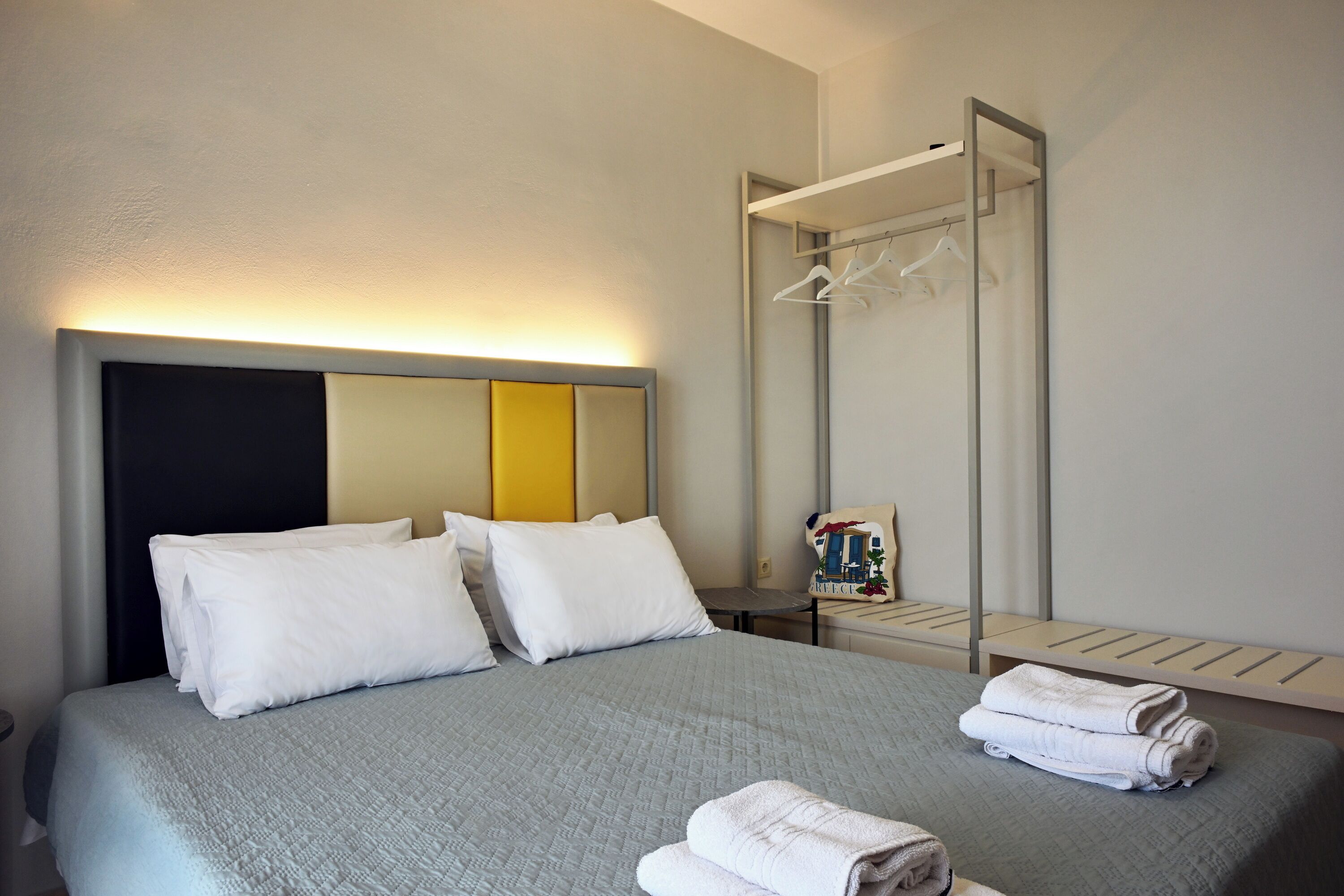 A neatly made bed with white pillows and a grey quilt, a bedside table with a book, and a wall-mounted towel rack.