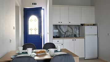 Ein Essbereich mit Tisch für zwei Personen, einer blauen Tür mit Fenster und weißen Schränken sowie einem weißen Kühlschrank.