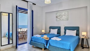 A hotel room with two beds, a balcony with a table and chairs, and a view of the sea. - Sfakian Horizon (Sfakia)