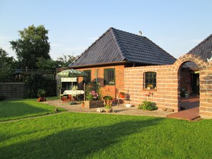 Ein Ziegelhaus mit einem Ziegeldach, eine Terrasse mit Tisch und Stühlen sowie ein Garten.