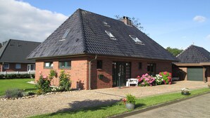 Een tweelaags bakstenen huis met schuin dak, een voordeur en een klein portaal met een stoel.
