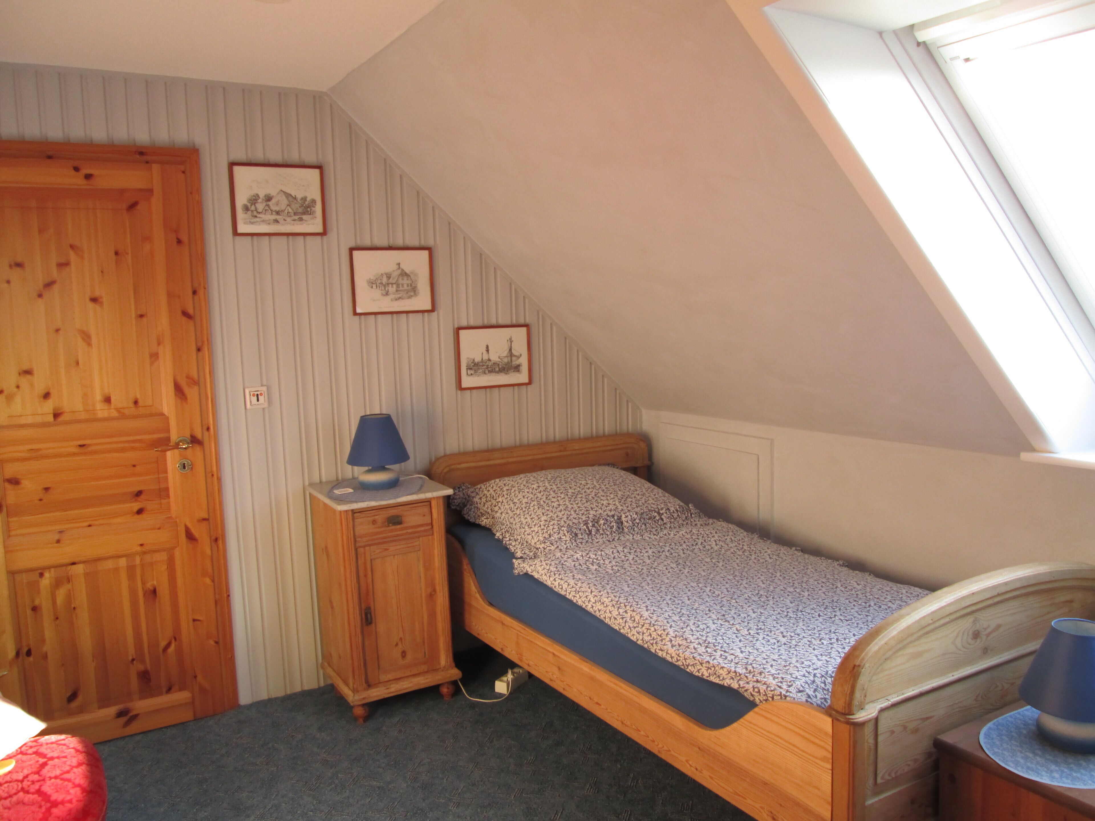 A small, cozy bedroom with a single bed, a nightstand, a wooden wardrobe, and a window providing natural light.