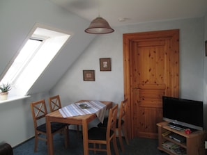 A dining area with a table, chairs, a television, and a wooden door.