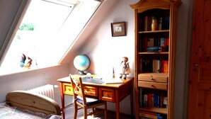 Een kamer met een houten bureau, een wereldbol, een boekenkast, een bed en een raam.