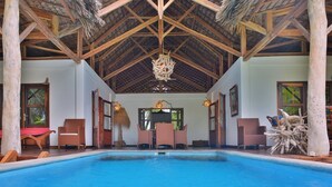 A pool area with a wooden ceiling and thatched roof, wicker furniture, and a hanging light fixture.