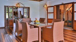 A dining area with wicker chairs and a glass table, featuring a fruit bowl.